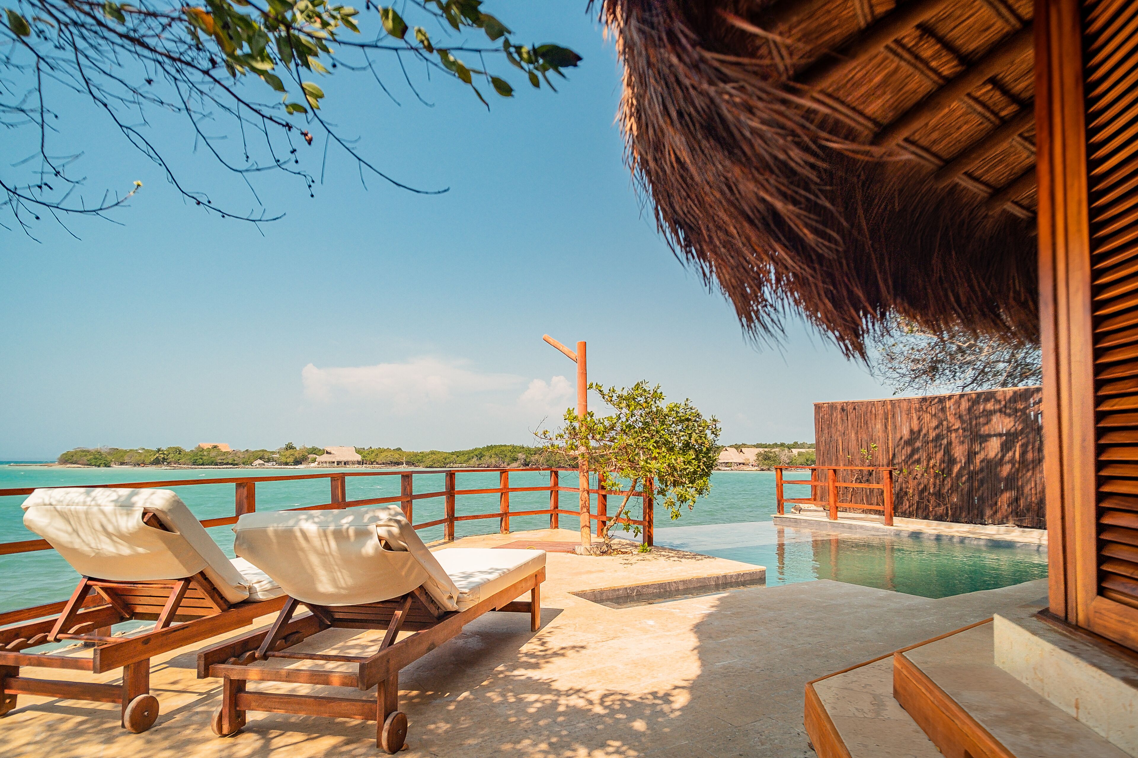 A poolside area with lounge chairs, a wooden fence, and a view of the ocean.