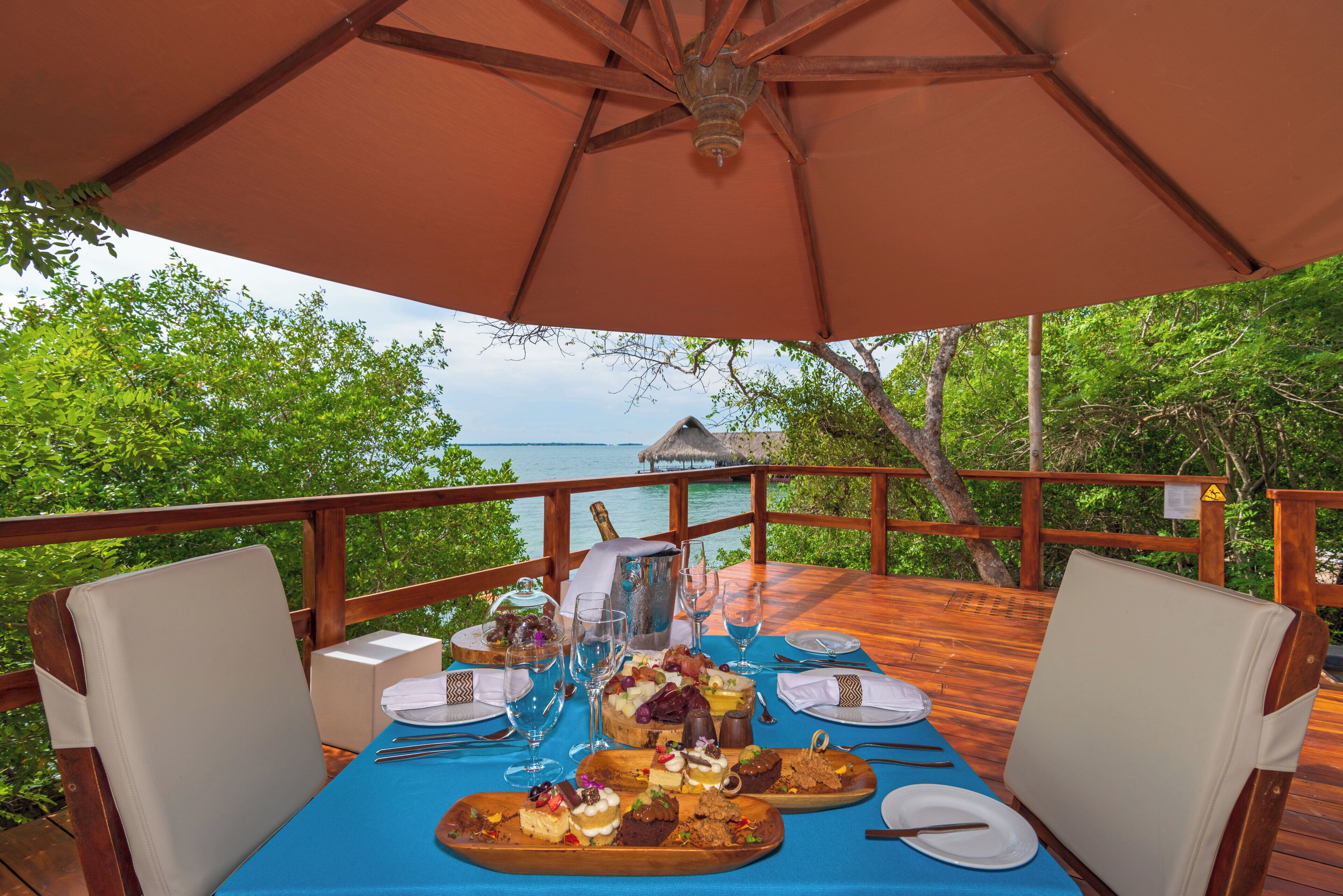 An outdoor dining area with a table set for two, overlooking a scenic view of the ocean and lush greenery.