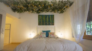 Un dormitorio con cama, un tapiz floral, un cuadro y una ventana con cortinas.