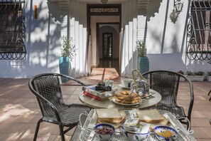 An outdoor dining area with wicker chairs, a round table, and a variety of food items including bread, condiments, and a teapot. - Gala Placida Experience 1923 (Granada)