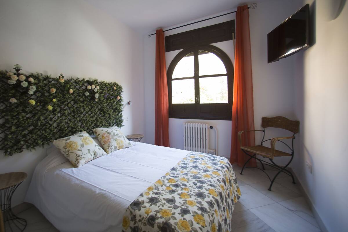 A bedroom with a bed, a radiator, a window with curtains, a television on the wall, and a chair.