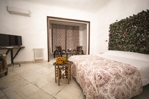 A bedroom with a bed, a television, a radiator, a table with chairs, and a floral wall decoration. - Gala Placida Experience 1923 (Granada)