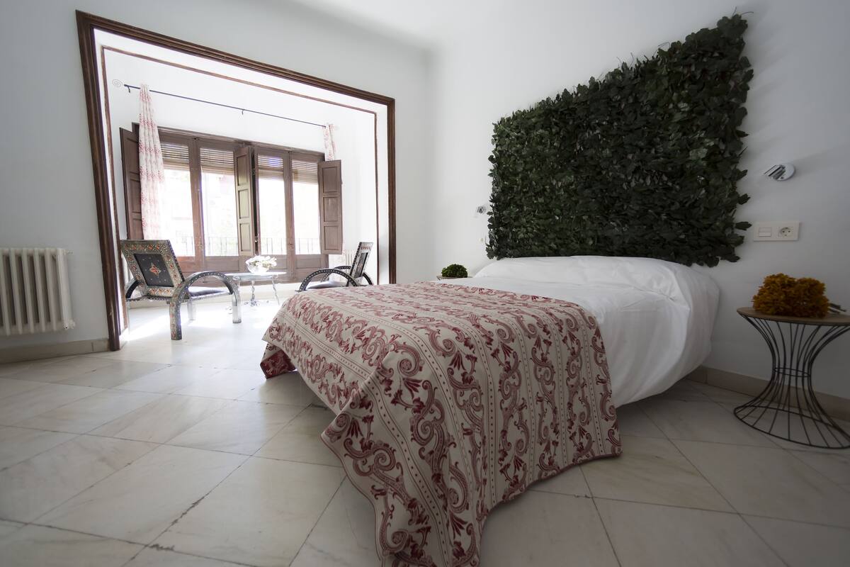 A bedroom with a bed, a small table with a plant, and a view of the outside balcony.
