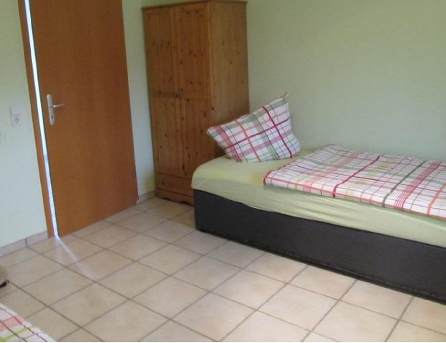 A bedroom with a bed, a wooden wardrobe, and a tiled floor.