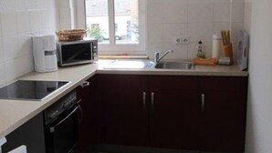 A compact kitchen with white tiles, a microwave, a sink, and a window with a view of the outside. - Apartment im Dresdner Amselgrund (Dresden)
