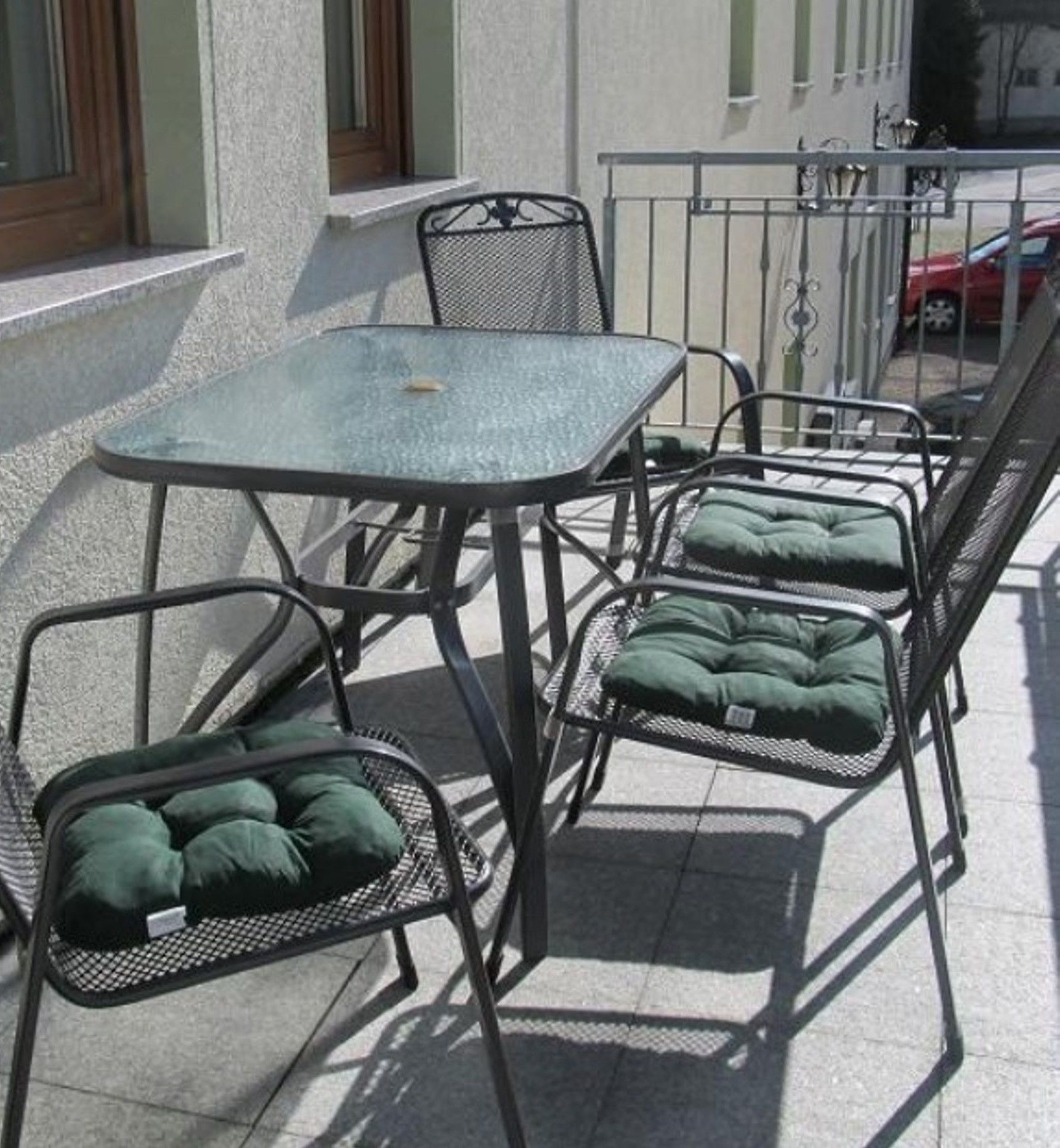 A small outdoor patio with a metal table and four chairs, each with a green cushion.