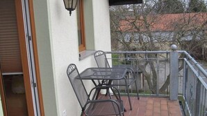 A balcony with a table and chairs, a window with a view of trees, and a door leading to an interior space. - Apartment im Dresdner Amselgrund (Dresden)