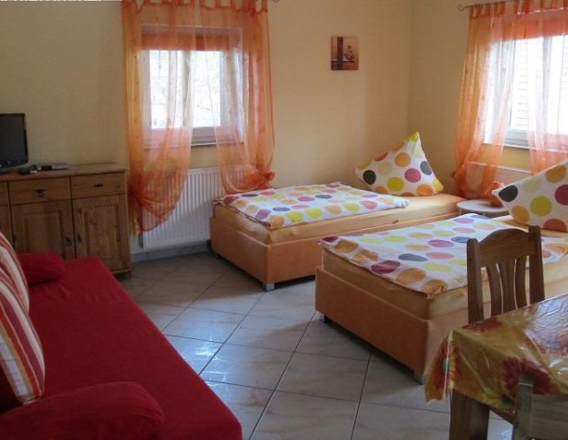 A room with two beds, a red sofa, a wooden cabinet, and a table with a tablecloth.