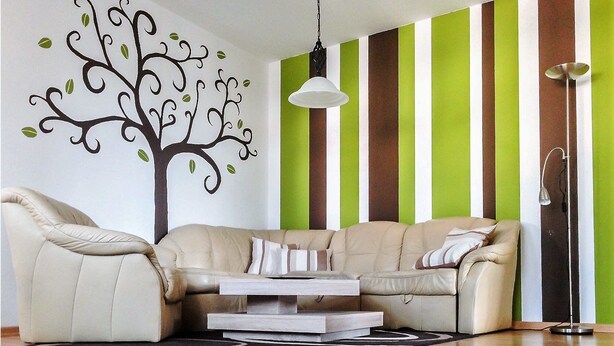 Una sala de estar con un sofá color crema, una mesita de centro, una pared a rayas y una calcomanía de un árbol.