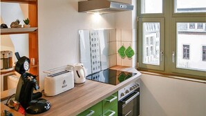 Una cocina con estufa, horno y varios electrodomésticos. Se aprecia una ventana con vistas a edificios.