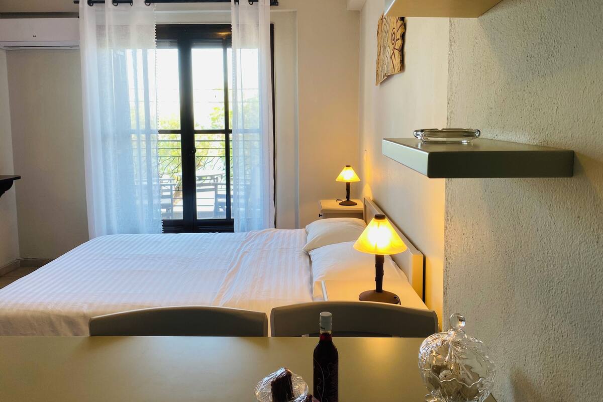 A hotel room with a bed, two bedside lamps, a bottle of wine, and a glass decanter on a table.