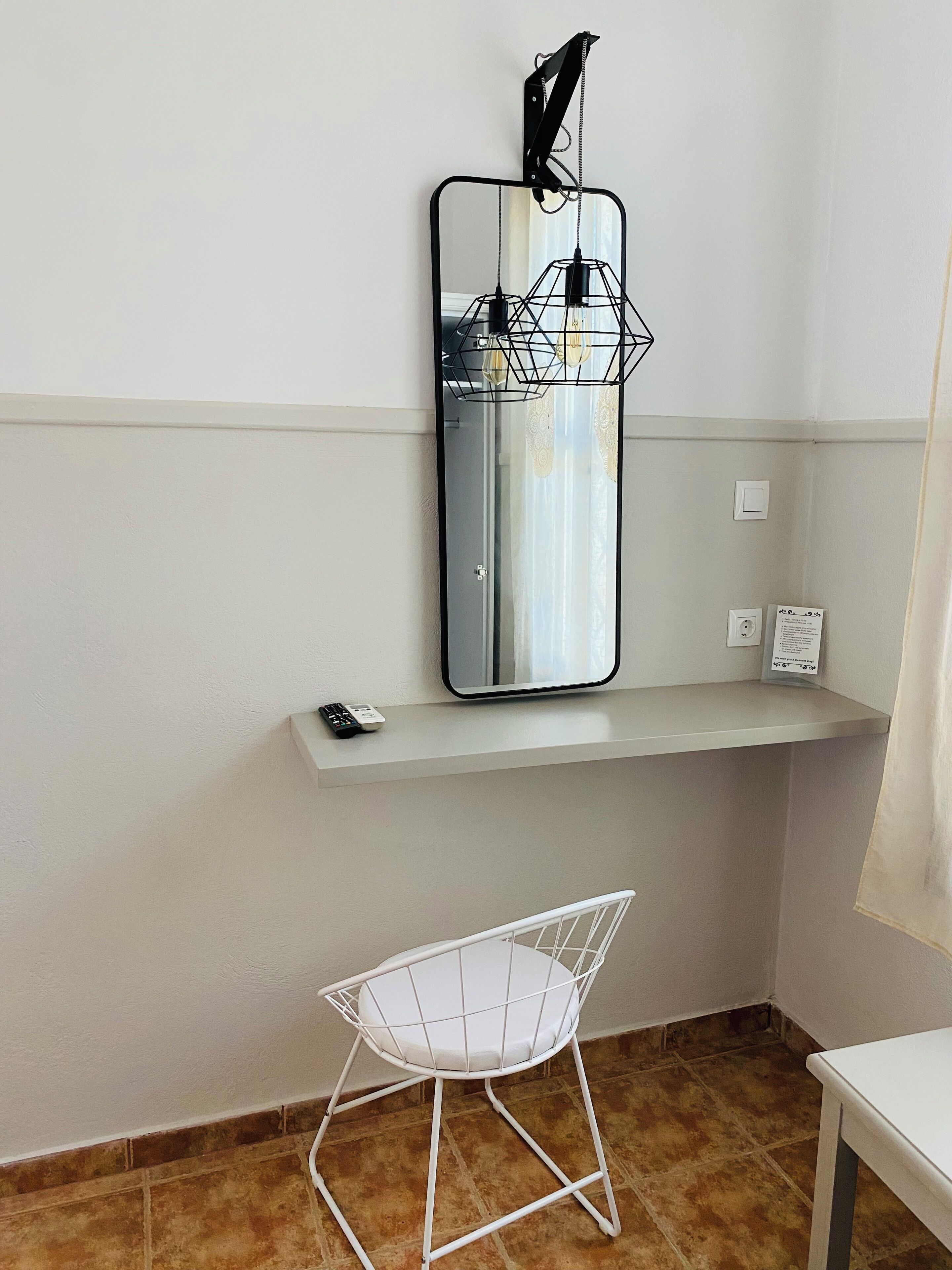 Een witte stoel met metalen frame, een witte plank met een afstandsbediening, en een wandspiegel met zwart frame.