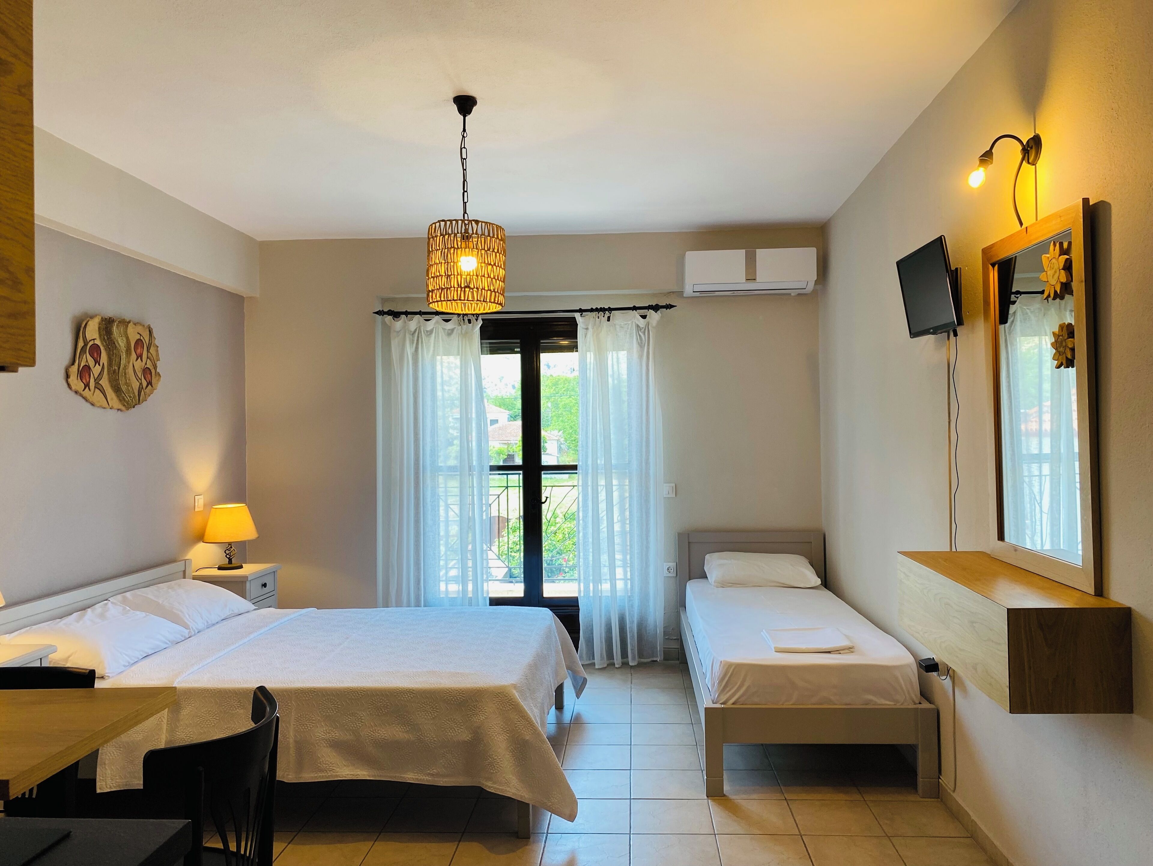 A hotel room with two beds, a desk, a chair, a lamp, a ceiling light, an air conditioner, a TV, and a window with curtains.