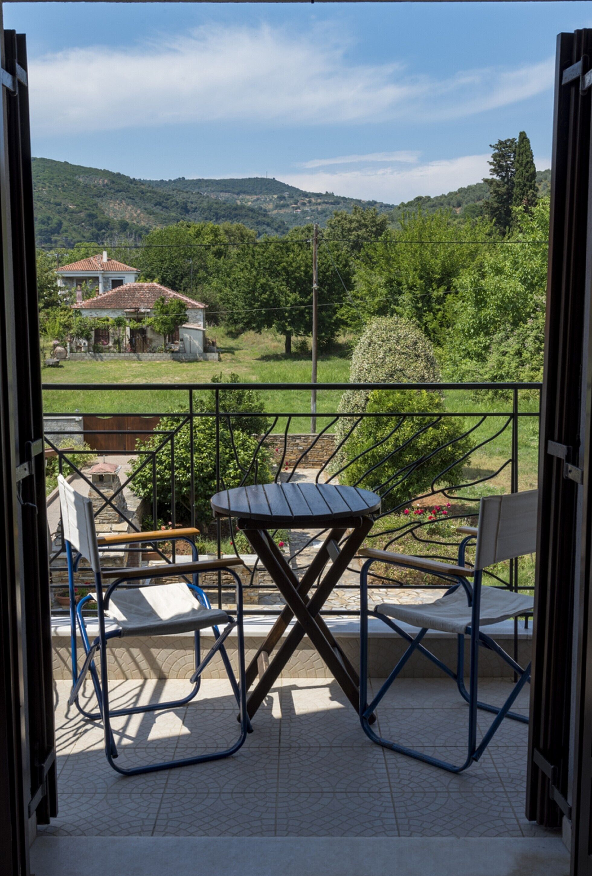 Un patio exterior con una mesa y sillas, y una vista de una casa y colinas al fondo.