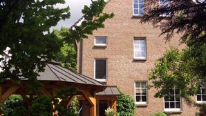 Een bakstenen gebouw met meerdere ramen, een overdekt buitengebied met een hangmat en een speeltuin.