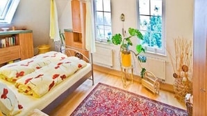 Een slaapkamer met een bed, een raam, een nachtkastje, een stoel en een plant.