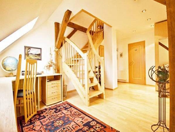 A spacious room with a wooden staircase, a desk with drawers, a globe, and a patterned rug.