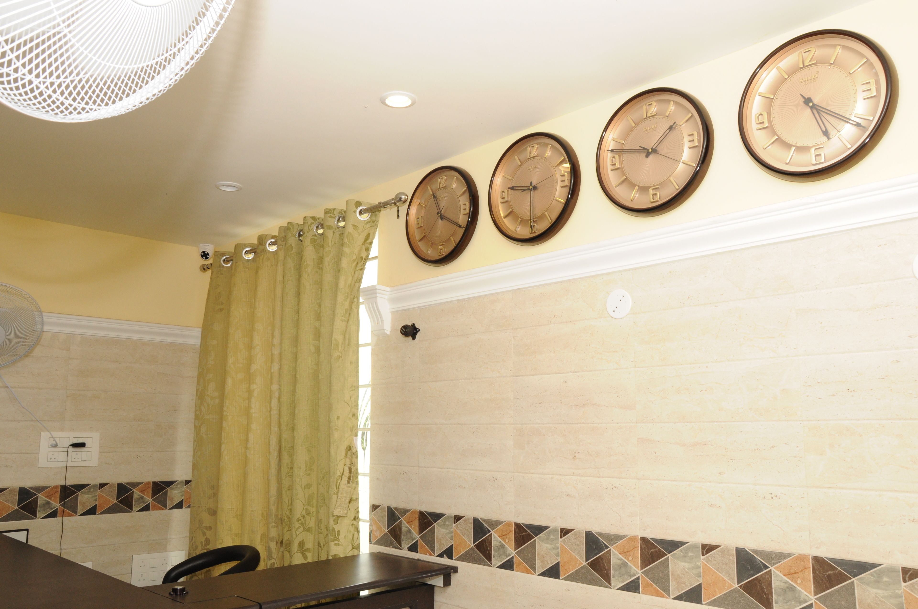 Un baño con tres relojes de pared, un ventilador y una cortina de ducha.