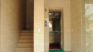 Un ascensor moderno con puerta de vidrio, un felpudo azul en la base y paredes con azulejos color beige.