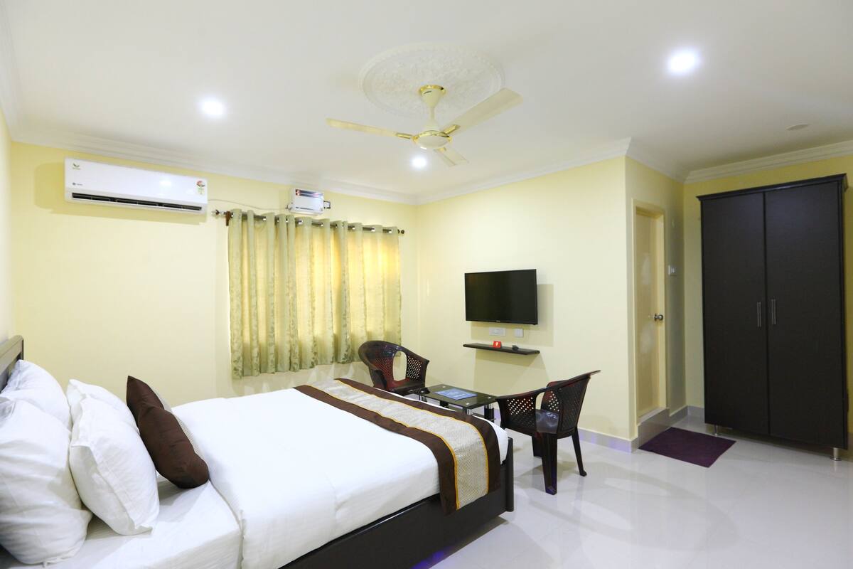 A hotel room with a bed, a desk, a chair, a television, an air conditioner, and a wardrobe.