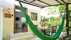 Une pièce avec un hamac vert, une table à manger avec des chaises et un escalier menant à une autre pièce.