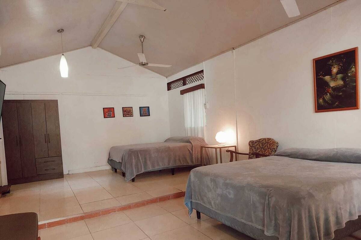 A room with two beds, a wardrobe, a ceiling fan, and a painting on the wall.