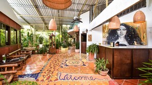 Un hall d’hôtel avec un sol en mosaïque, des meubles en bois et des plantes en pot.