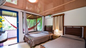 Une chambre avec deux lits, une petite table, un ventilateur et une fenêtre donnant sur un paysage verdoyant.