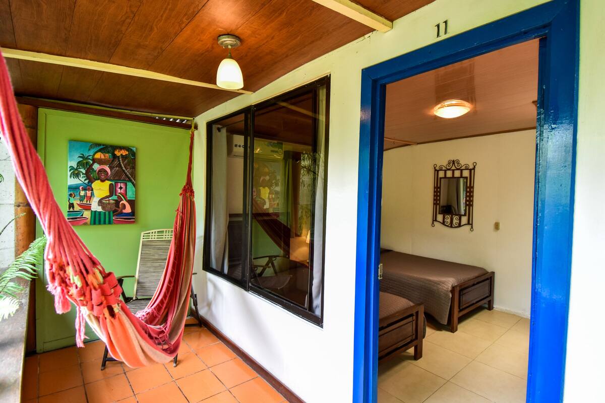 A room with a hammock, a bed, a window, and a painting on the wall.