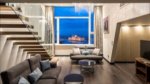 A modern living room with a staircase, a sofa set, a coffee table, and a view of a cityscape at night. - Castle Apartments Budapest (Budapest)