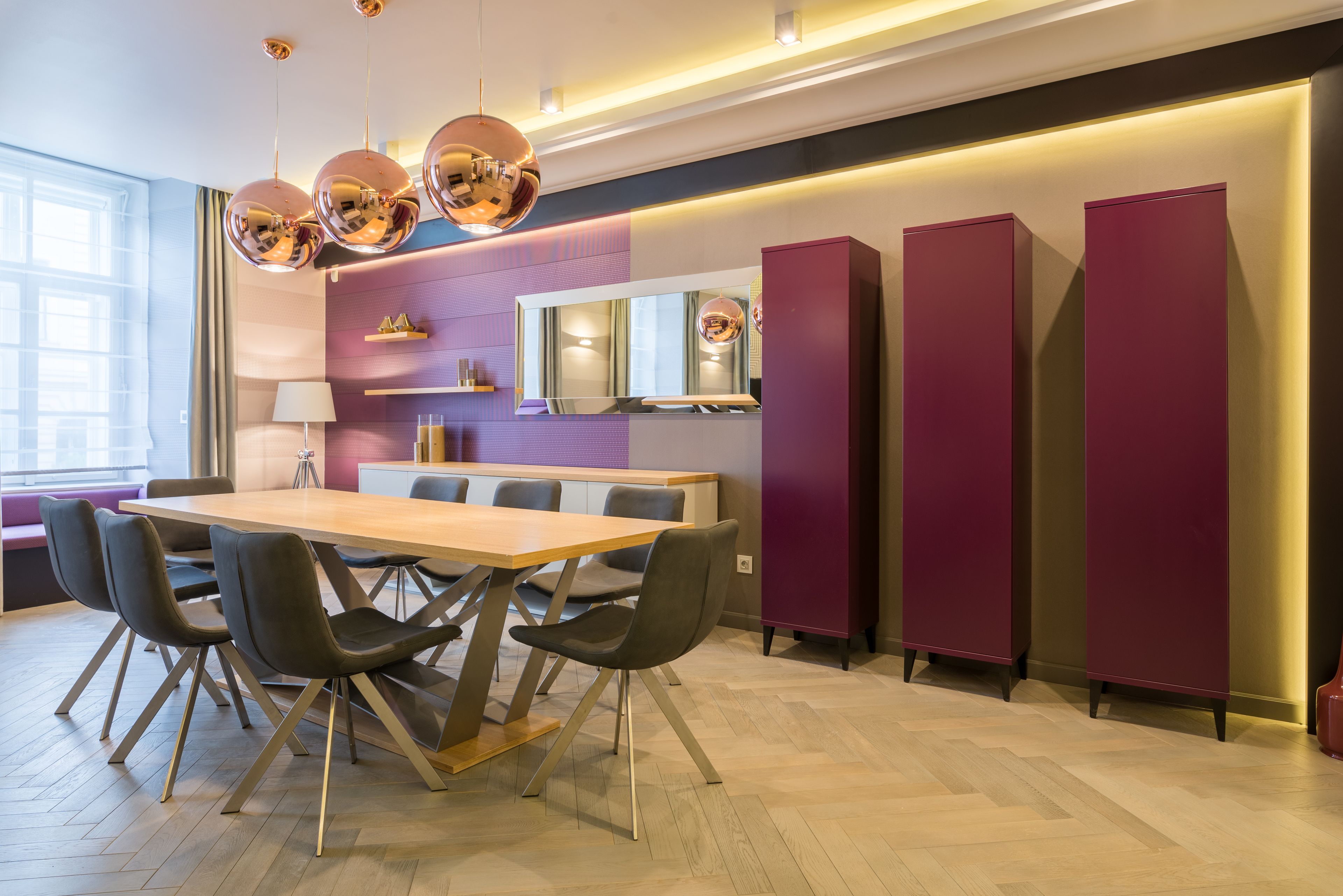 A modern dining area with a wooden table, black chairs, and a large mirror above.