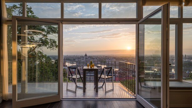 A modern room with a large glass door leading to an outdoor balcony with a table and chairs, offering a city view. - Castle Apartments Budapest (Budapest)