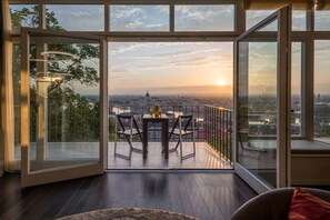 A modern room with a large glass door leading to an outdoor balcony with a table and chairs, offering a city view. - Castle Apartments Budapest (Budapest)