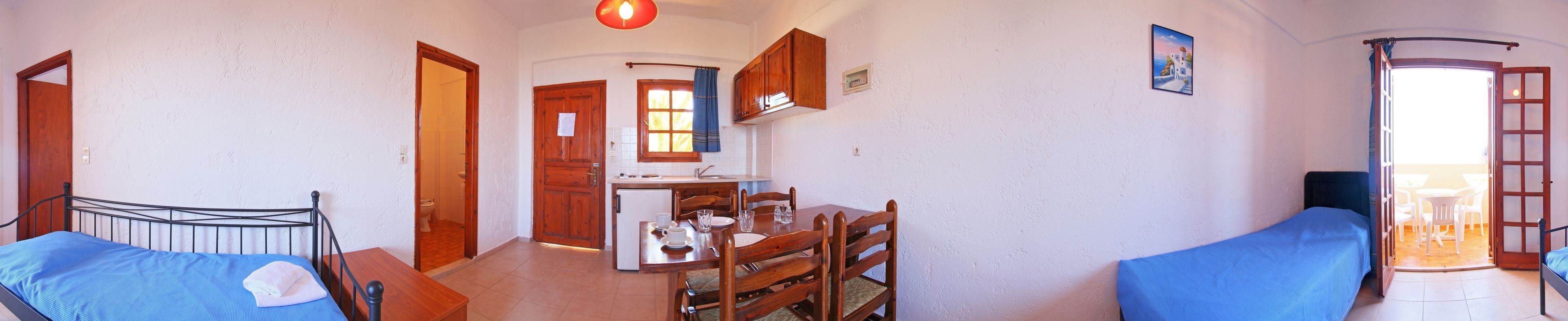 Ett rum med en säng, ett matbord med stolar, en köksdel och en balkong med ett bord och stolar.