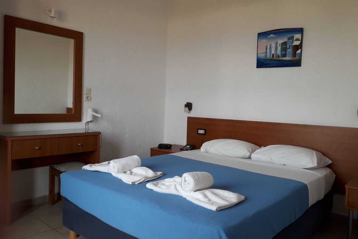 A hotel room with a large bed, a wooden headboard, a desk with a mirror, and a painting on the wall.