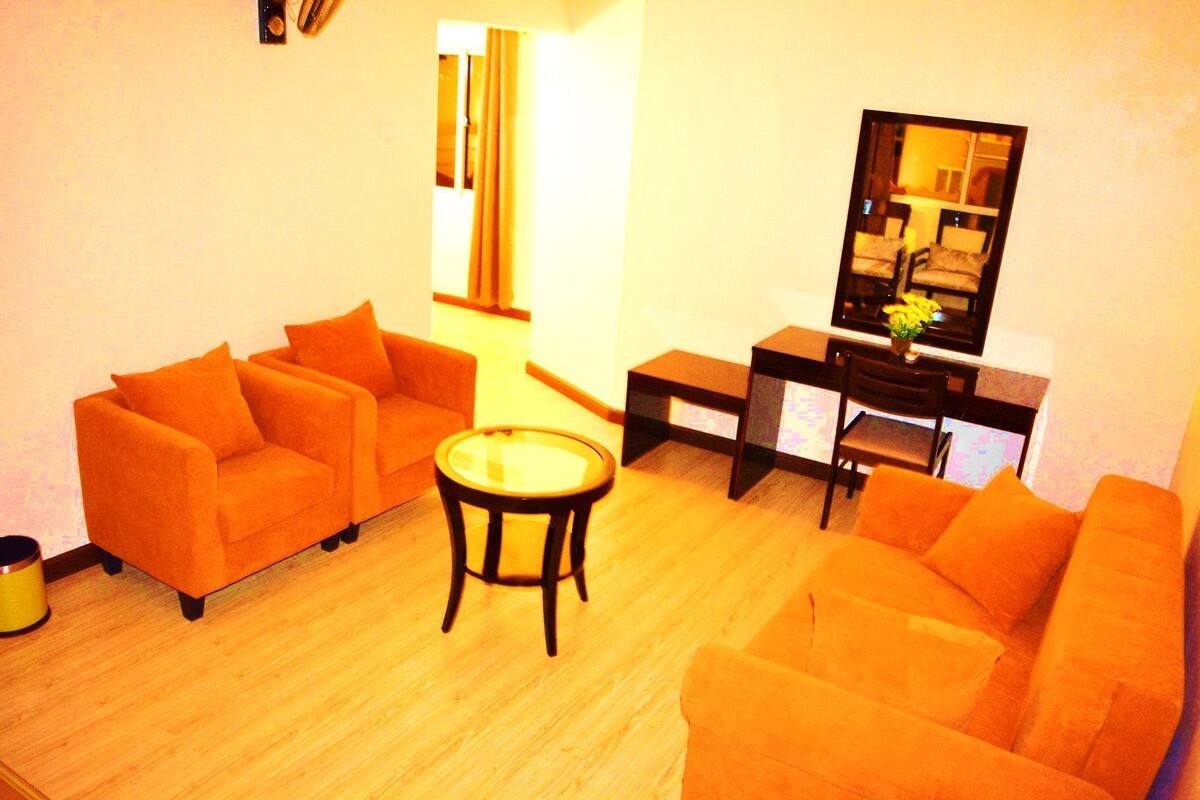 A living room with two orange sofas, a small round table, and a TV stand with a flat-screen TV.