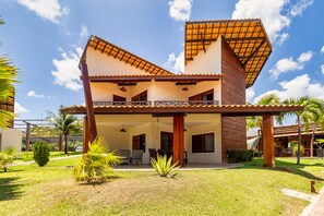 Uma casa de dois andares com varanda coberta, gramado e palmeiras.