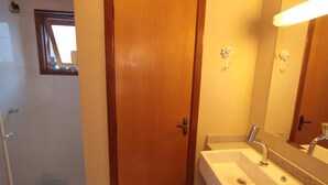 A bathroom with a wooden door, a sink with a mirror, and a shower area. - Cabana Belo Destino (Gramado)