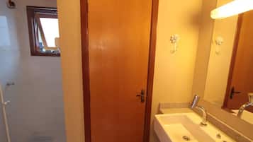 Uma casa de banho com porta de madeira, pia com espelho e zona de duche.