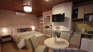 A hotel room with a bed, bedside tables, a TV, a dining table with chairs, and a kitchen area. - Cabana Belo Destino (Gramado)