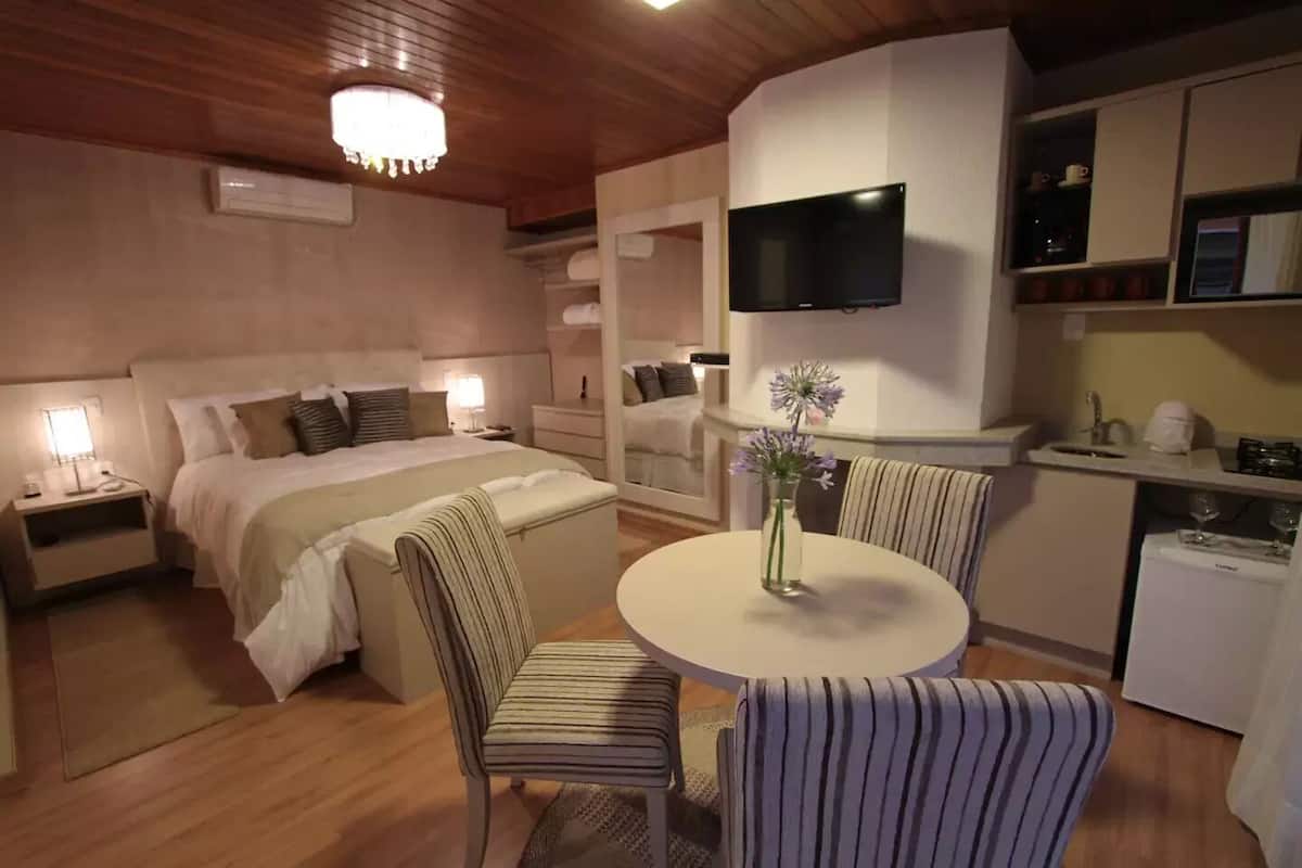 Une chambre d’hôtel comprenant un lit, des tables de chevet, une télévision, une table à manger avec des chaises et un coin cuisine.