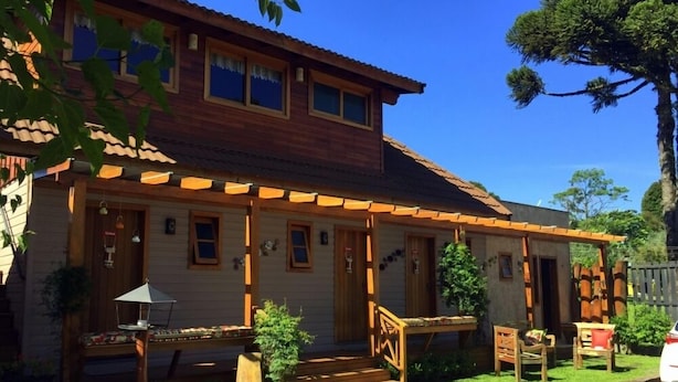 A two-story wooden house with a porch, a small garden, and a car parked in front. - Cabana Belo Destino (Gramado)