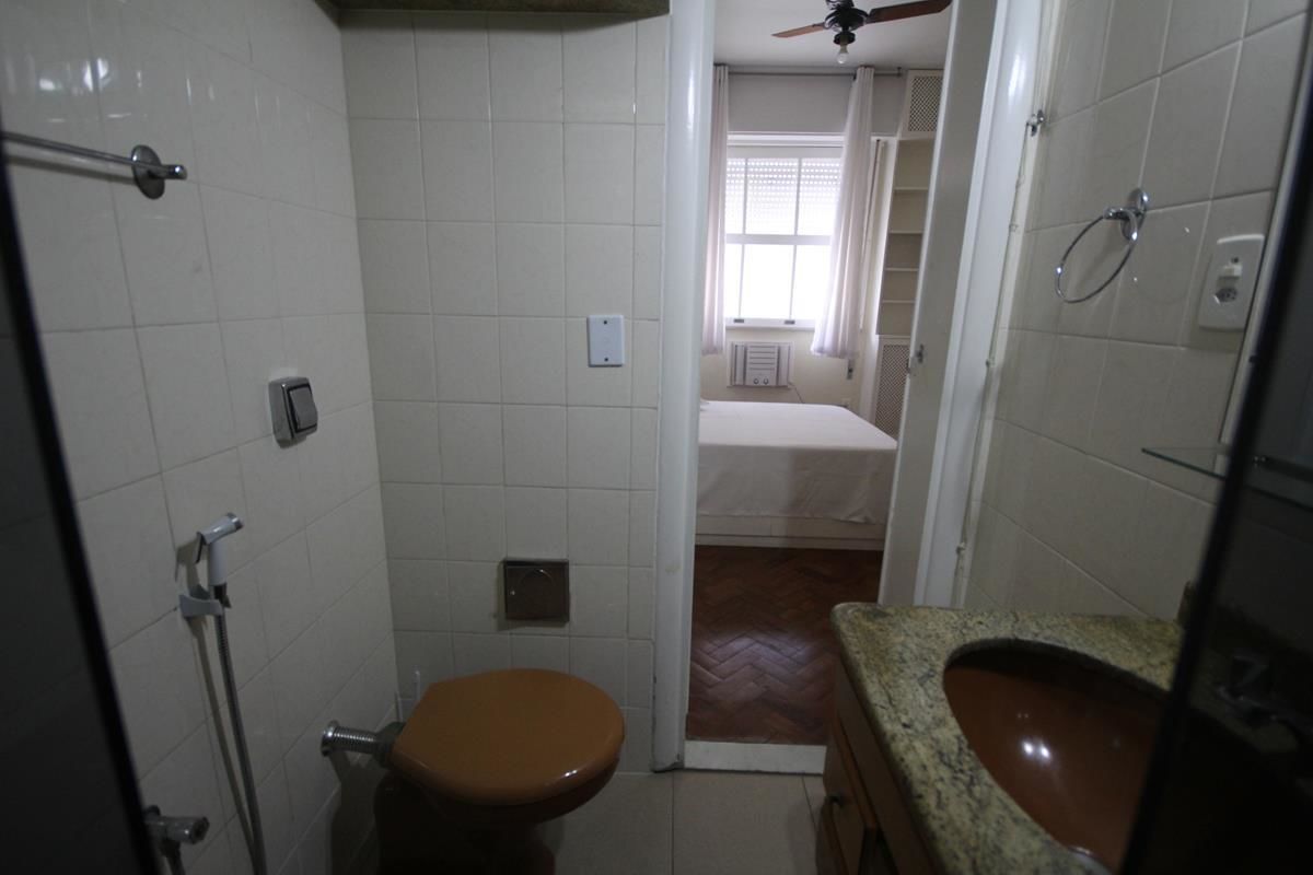 A bathroom with white tiled walls, a brown toilet, a shower area, and a sink with a granite countertop.