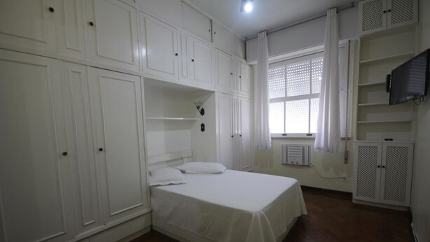 Een slaapkamer met een bed, een witte garderobe en ingebouwde planken.