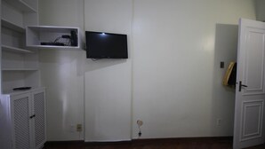 Een kamer met een flatscreen televisie aan de muur, een witte deur en een wit kastje met een plank.