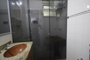 A bathroom with a glass-enclosed shower, a granite sink, and a white tiled wall.