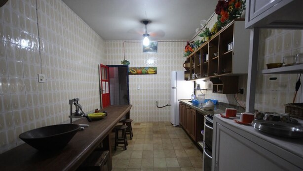 A kitchen with white tiled walls, a wooden countertop, and a sink. There is a ceiling fan, a refrigerator, and cabinets above the counter. - GoHouse Torre 16 (Rio de Janeiro)