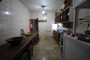 Une cuisine avec des murs recouverts de carreaux blancs, un plan de travail en bois et un évier. On y trouve également un ventilateur de plafond, un réfrigérateur et des placards au-dessus du plan de travail.