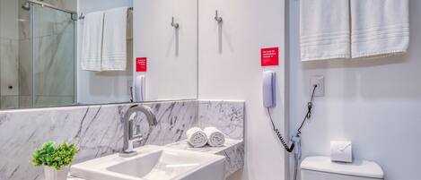 Un baño moderno con lavamanos de mármol, dos toalleros, una cabina de ducha de cristal y un inodoro con dispensador de toallas de papel.