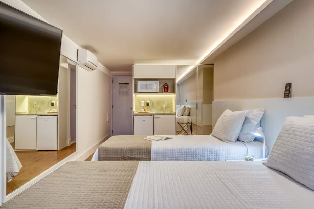 Ein Hotelzimmer mit zwei Betten, einer Küchenzeile und einem kleinen Badezimmer.